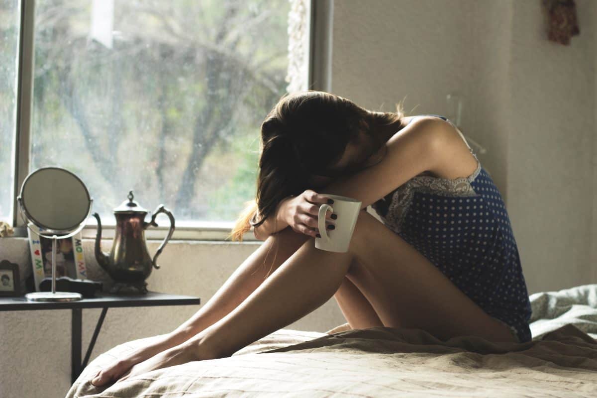 depressed woman sitting on the bed, holding a mug