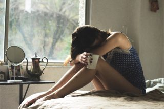 depressed woman sitting on the bed, holding a mug