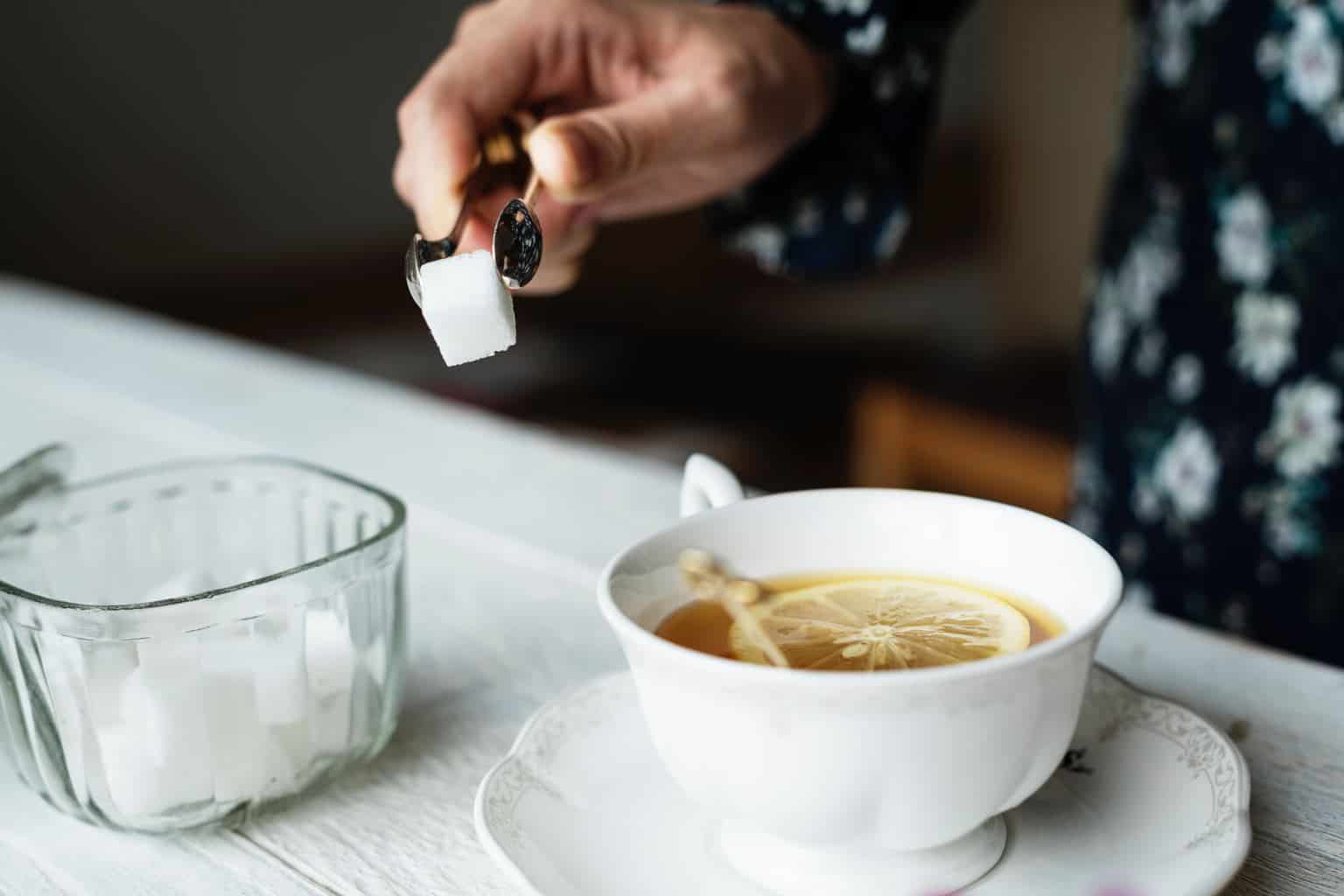person transferring cube of sugar to teacup
