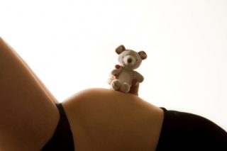 pregnancy woman laying with a stuffed teddy bear on her belly